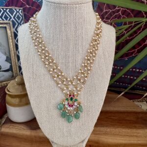 Three-layer pearl necklace with a Jadau Kundan floral pendant and emerald-green stone drops.