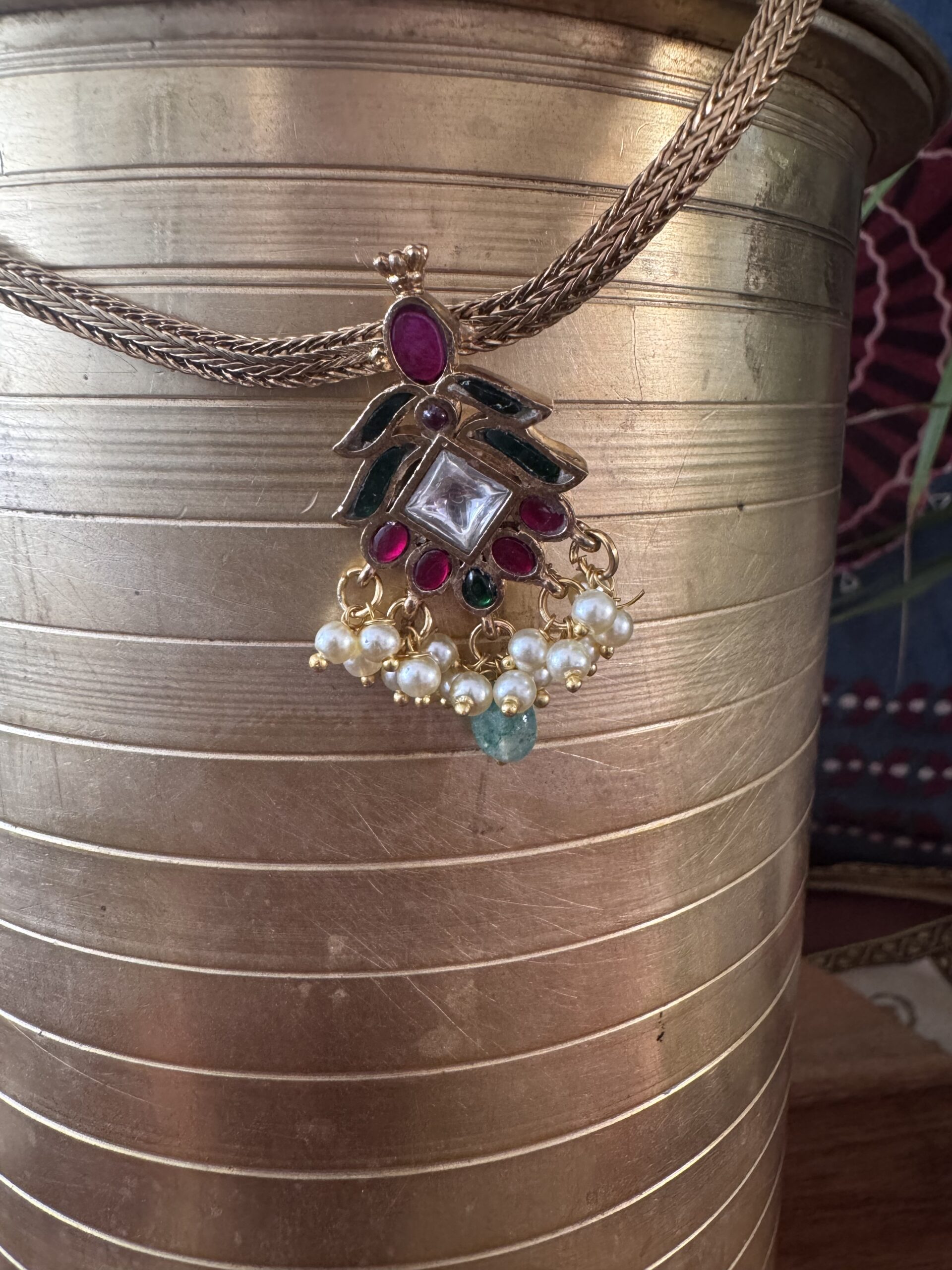 Gold-toned necklace with a pink and green Kundan pendant and pearl drops.