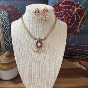 Gold-toned necklace with a pink and green Kundan pendant and pearl drops.
