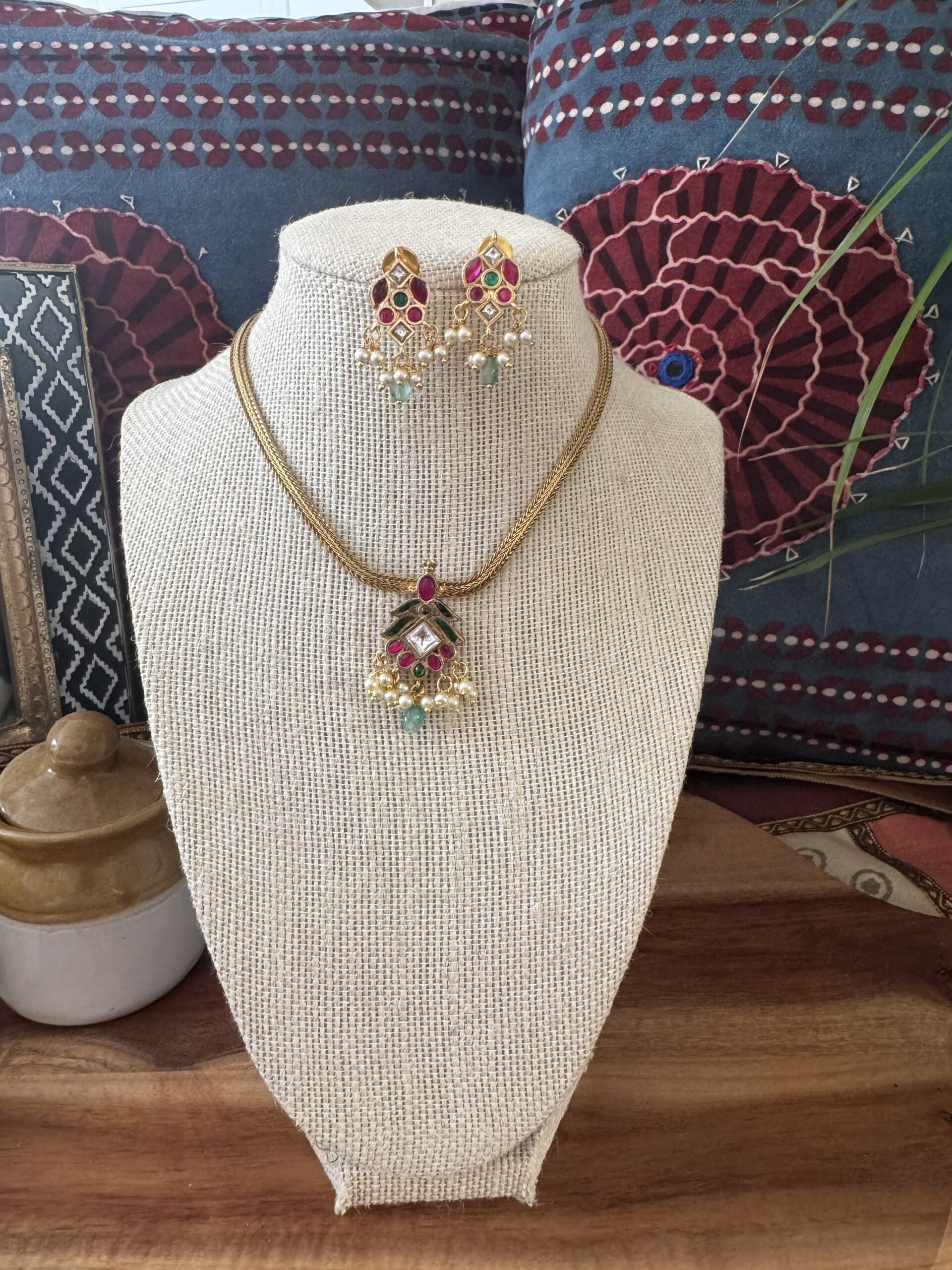 Gold-toned necklace with a pink and green Kundan pendant and pearl drops.