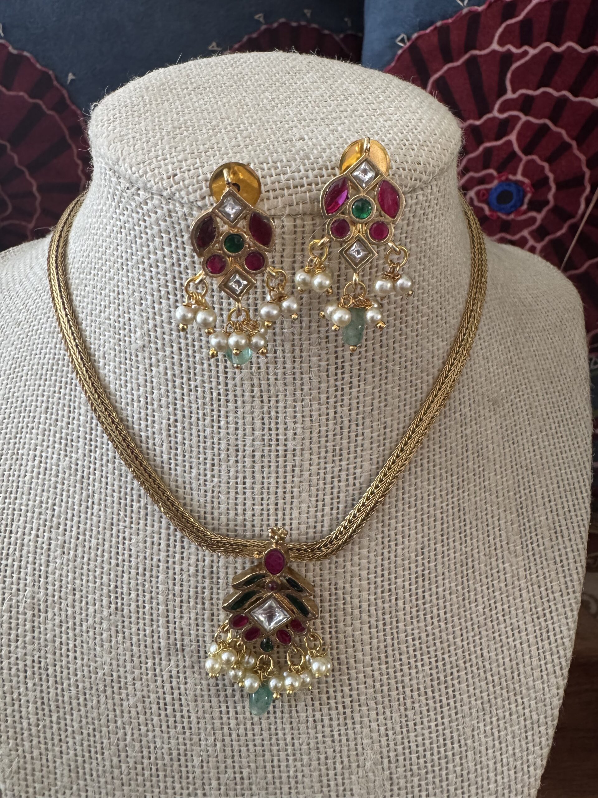 Gold-toned necklace with a pink and green Kundan pendant and pearl drops.