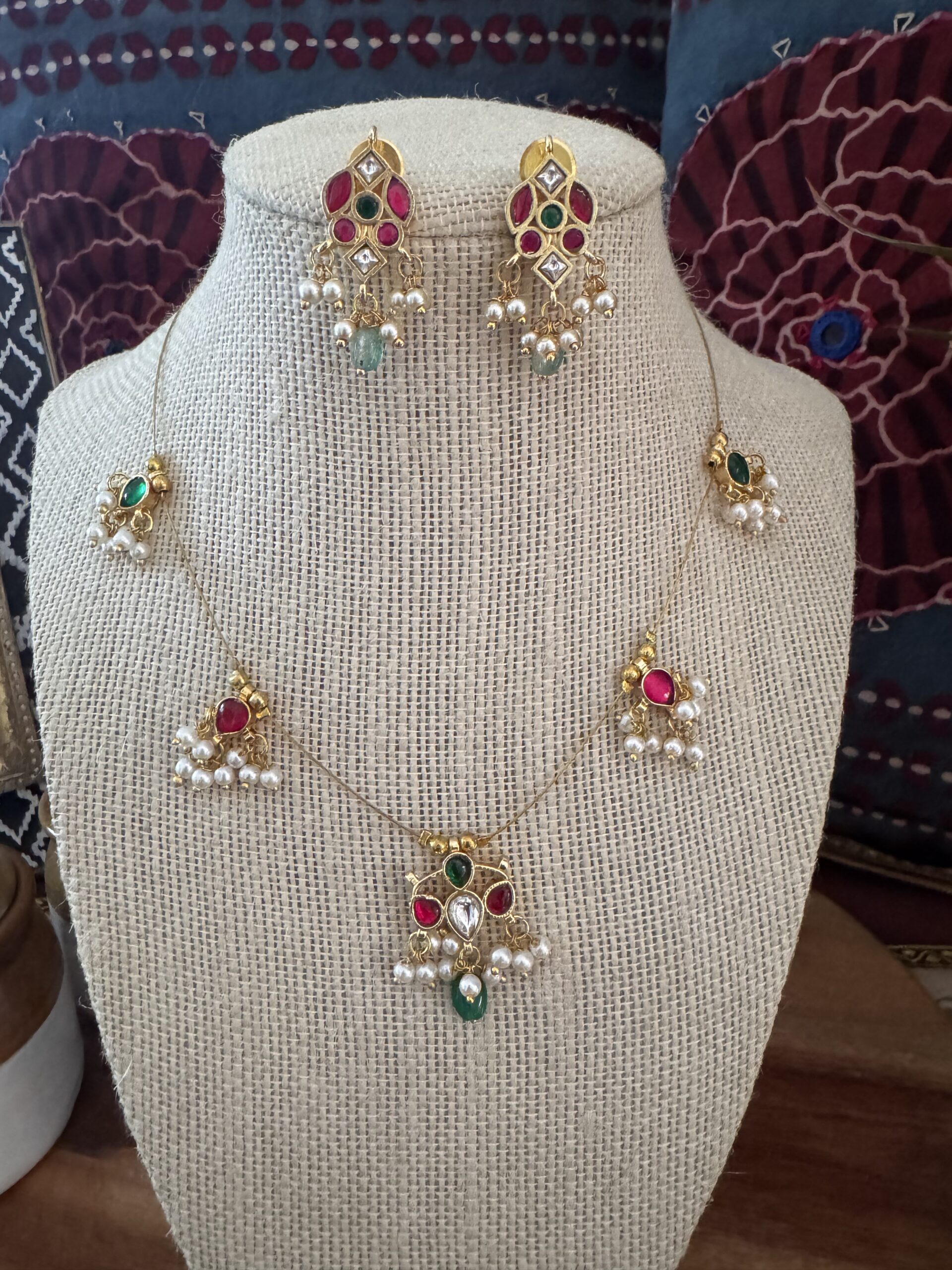 Gold-toned Kundan necklace with red and green stone charms and pearl drops on a white background.