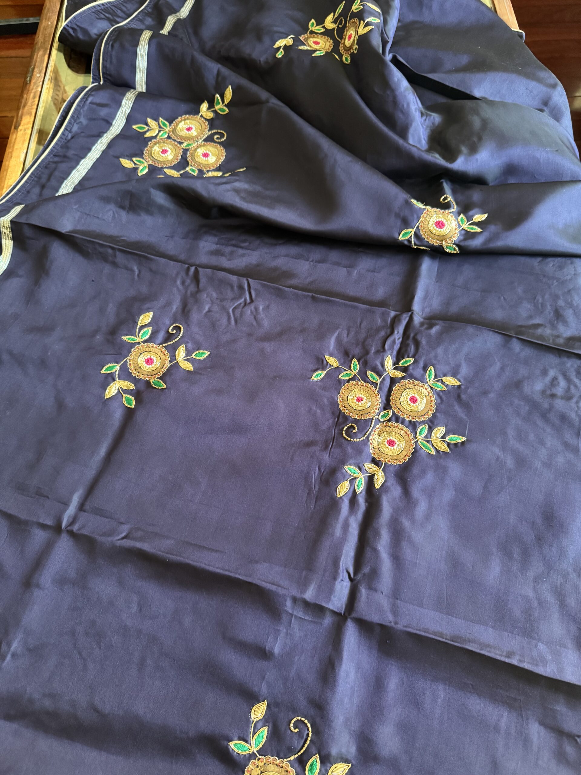 Close-up of hand-embroidered gold zari floral cluster on Indranila midnight blue pure silk saree — circular blooms with pink centres and emerald green leaves — Tari by Gayatri