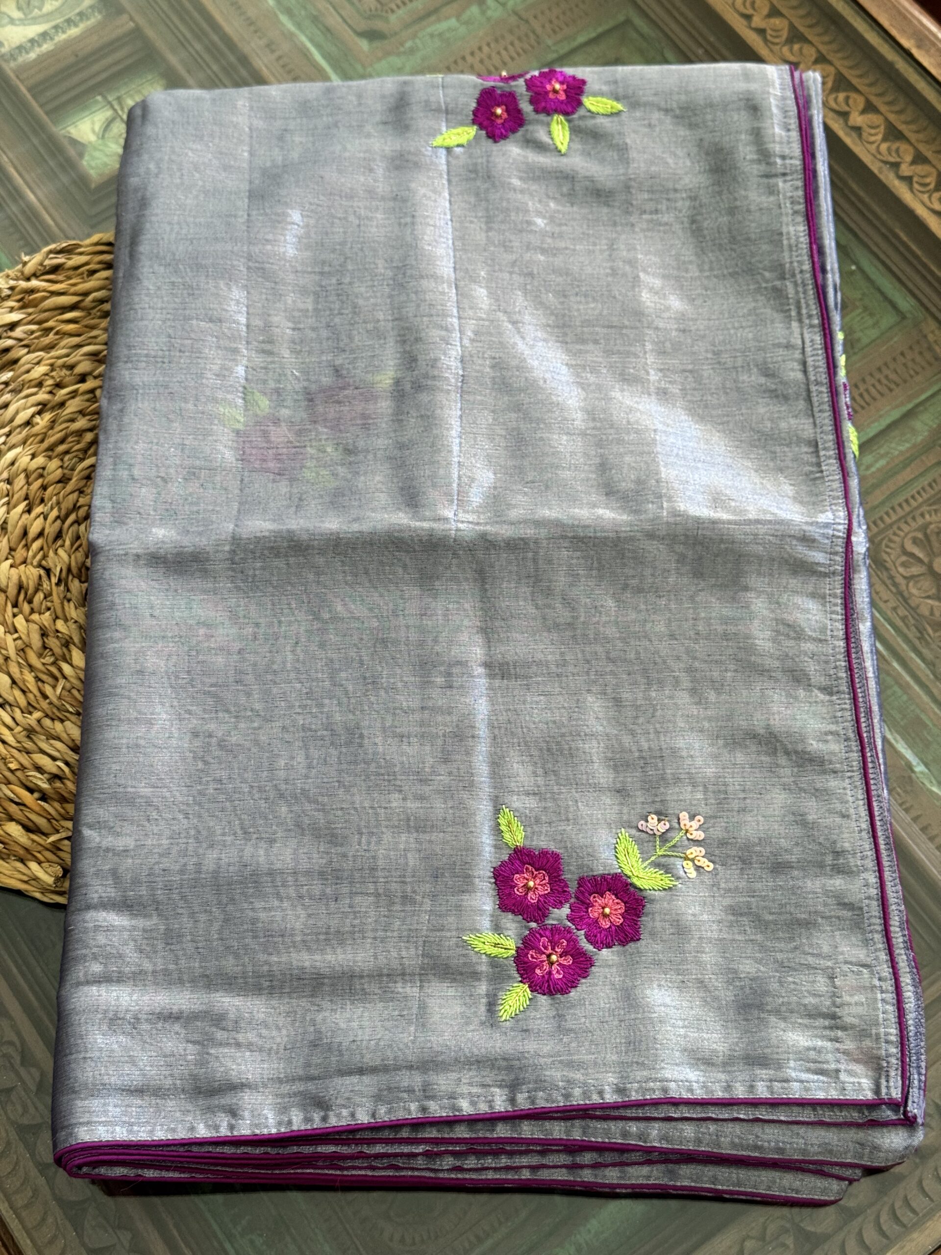 Shubhra silver-grey handwoven tissue silk saree folded, showing scattered hand-embroidered magenta floral sprigs with lime green leaves and fuchsia piping trim — Tari by Gayatri