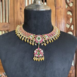 UUKA traditional gold toned Jadau necklace with pink and green stones and matching jhumki earrings on a black mannequin display