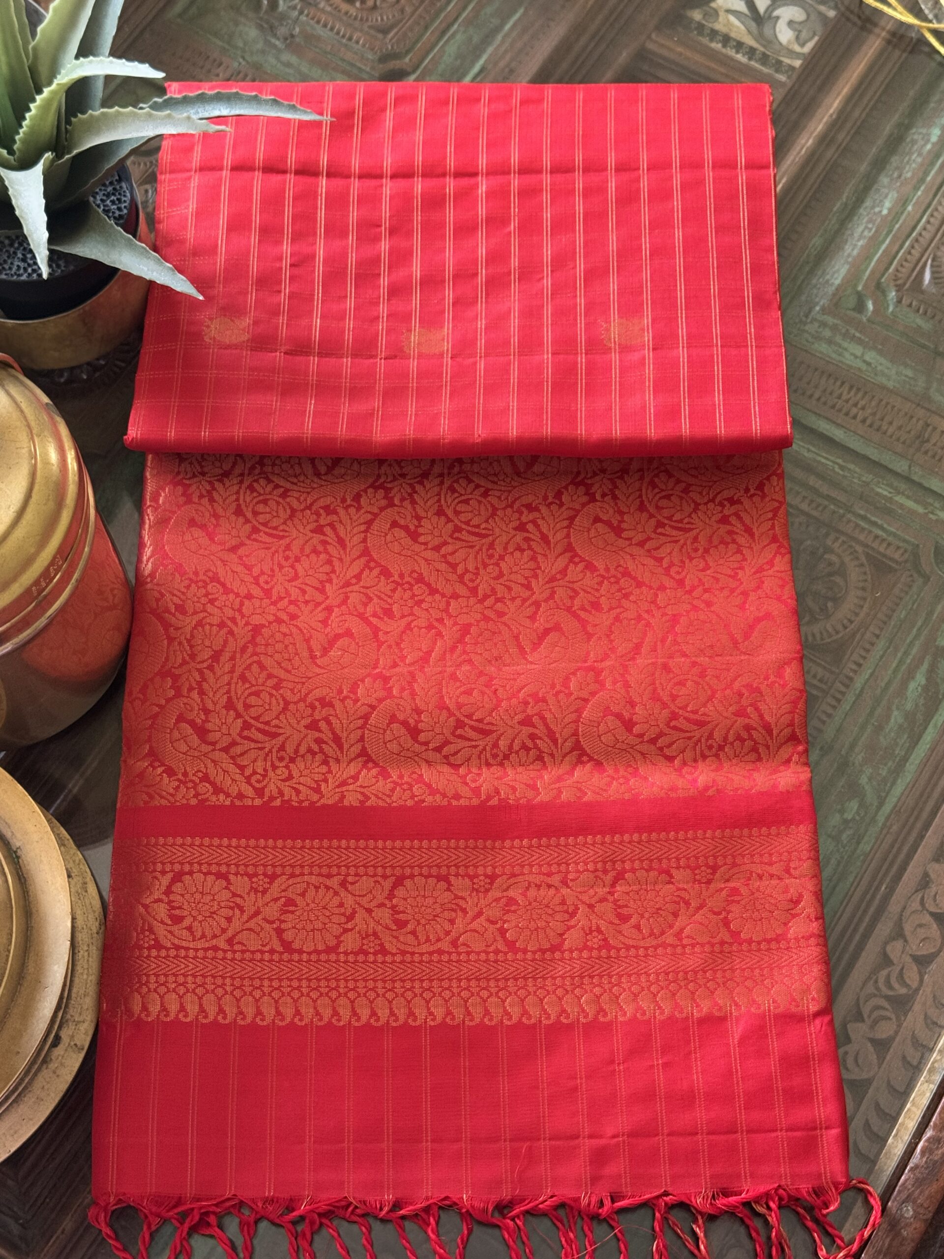 Nandini tomato red soft silk saree with gold zari checks and a peacock pallu with tassels.